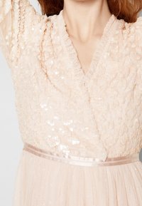 Abito rosa pallido con corpetto decorato da paillettes, scollatura arricciata e fascia in satin in vita, maniche lunghe trasparenti e gonna in tulle.