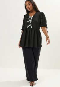 Top peplum nero con maniche a sbuffo, tessuto texturizzato e dettagli in nastro bianco. Abbinato a pantaloni neri larghi e sandali con cinturini.