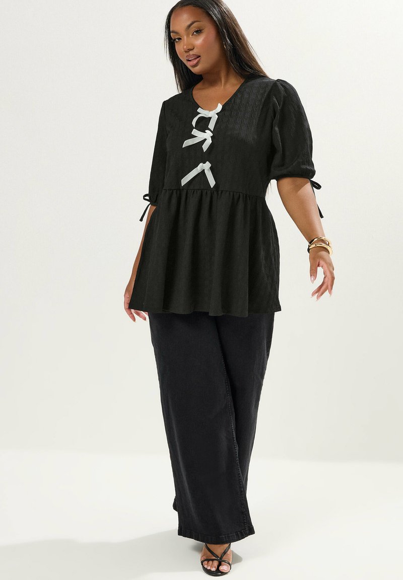 Top peplum nero con maniche a sbuffo, tessuto texturizzato e dettagli in nastro bianco. Abbinato a pantaloni neri larghi e sandali con cinturini.