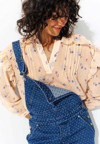 Les salopettes en denim présentent un motif bleu avec des pois bleu clair, superposées à un blouse en fleurs pêche avec des manches à volants et un détail plissé.