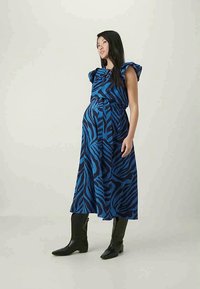 Φουστάνι με σχέδιο zebra σε μπλε και μαύρο, με ρίγες στα μανίκια, σφιχτή μέση και ρέουσα μεσαίου μήκους, συνδυασμένο με μαύρες μπότες μέχρι το γόνατο.