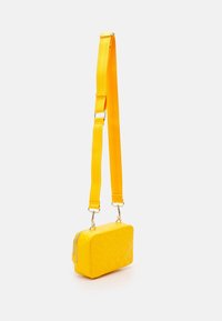 Borsa rettangolare gialla con superficie texturizzata, tracolla regolabile e hardware tono oro. Presenta una chiusura con zip e un motivo geometrico.
