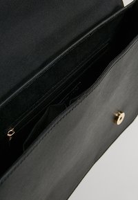 Borsa a mano nera in pelle con una texture liscia, dotata di una patta frontale con una chiusura a scatto color oro e di una tasca interna con zip.