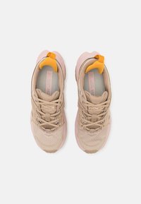 Lys beige joggesko med rosa detaljer, overdel i mesh og syntetisk materiale, rund tå, snøringssystem og en gul løkke bak på hælen.