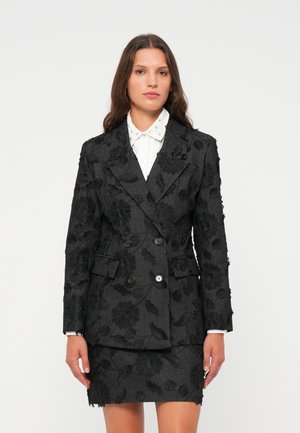 Svart blazer med blomsterbroderi, doble knapper og to frontlommer, kombinert med et matchende blyantskjørt. Struktursk stoff.