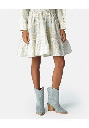 Mujer con un vestido corto de encaje crema de manga larga y botas de estilo vaquero gris de ante, con tacones de madera.