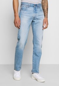 Jeans de mezclilla azul claro con corte recto, cinco bolsillos y herrajes metálicos. Combinados con zapatillas blancas. Tela suave y texturizada.