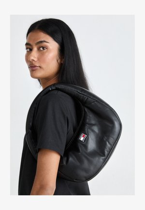 Zwarte leren rugzak met een ronde vorm, voorzien van een ritssluiting en een klein logo-opdruk in blauw, rood en wit.