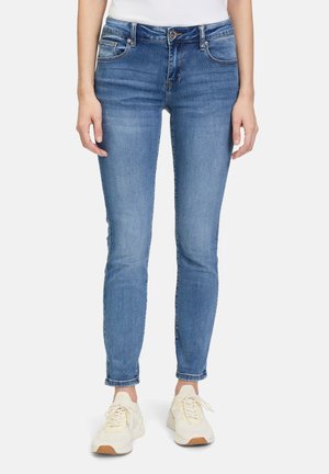 Jeans in denim blu skinny-fit con una leggera sbiaditura, design a cinque tasche, apertura con zip frontale e risvolti, abbinati a calzature bianche e beige.