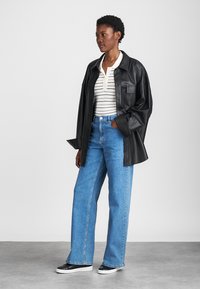 Μαύρο δερμάτινοOversized πουκάμισο, άσπρο πουκάμισο με ρίγες, μπλε ίσια τζιν παντελόνι και μαύρα-άσπρα αθλητικά παπούτσια. Λείο υλικό, χαλαρός σχεδιασμός.