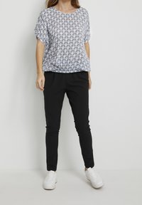 Top leggero a maniche corte con un motivo a ventaglio bianco e blu navy, abbinato a pantaloni neri attillati e sneakers bianche. Tessuto dalla texture liscia.