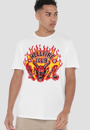 Weißes Baumwoll-T-Shirt mit einem farbenfrohen "Hellfire Club"-Motiv, das Flammen und ein rotes Totenkopf-Design zeigt, akzentuiert durch gekreuzte Waffen.