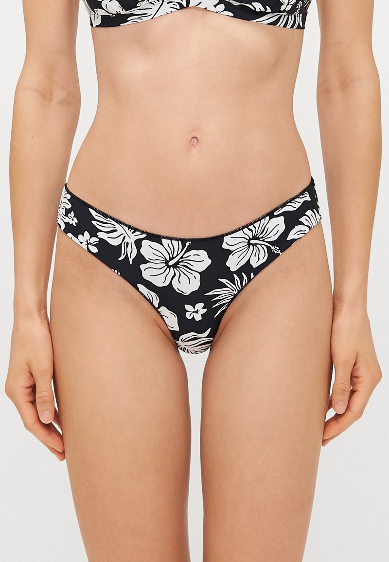 Melna bikini apakšda ar baltām ziedu rakstām, zemu jostas līniju un gludu, elastīgu audumu. Akcentēta ar kontrastējošām šuvēm.