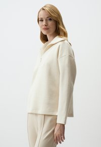 Hellbeige, mit Reißverschluss versehenes Sweatshirt aus weichem Stoff. Verfügt über einen strukturierten Kragen, einen lockeren Schnitt und lange Ärmel mit Rippbündchen.