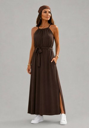Femme portant une robe maxi marron foncé sans manches avec une ceinture à la taille, une fente latérale, un bandeau assorti, des bijoux en or et des baskets blanches.