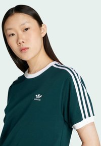 Green cotton T-shirt with white accents, featuring short sleeves, a round neckline, and a small white Adidas logo on the chest.