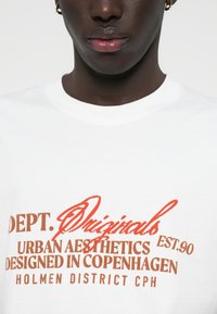 Biała koszulka z grafiką tekstu w brązowym i czerwonym kolorze, z napisem "Dept. Originals," "Urban Aesthetics" oraz "Designed in Copenhagen."
