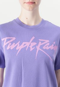 Purple cotton t-shirt featuring a bold, stylized "Purple Rain" graphic in light pink across the front, round neckline, and short sleeves.