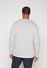 Langärmliges, hellgraues Shirt aus weichem Material, mit Rundhalsausschnitt und schmaler Passform, die eine dezente Struktur und seitliche Schlitze am Saum aufweist.