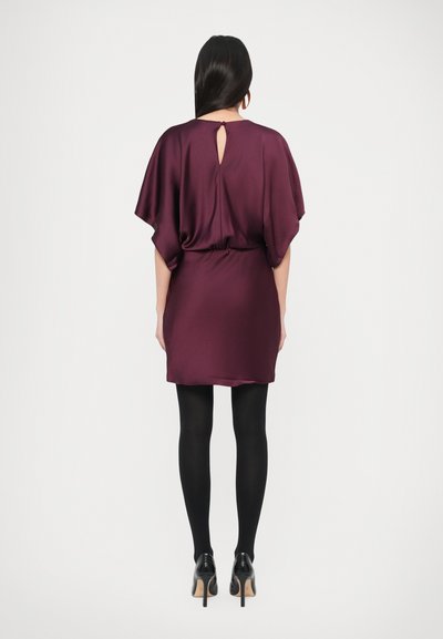 Rochie scurtă din satin într-o nuanță bogată de burgund, cu spate decupat, mâneci largi și talie elastică, asortată cu colanți negri și tocuri.