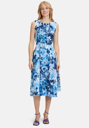 Ein ärmelloses, knielanges Kleid mit einem blauen Blumenmuster in verschiedenen Schattierungen. Der Stoff hat eine glatte Textur, eine taillierte Taille und einen schwingenden Rock.