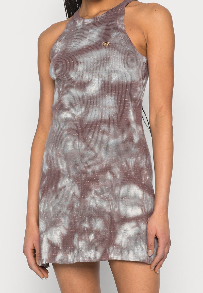 Robe sans manches, moulante, à effet tie-dye violet et blanc, avec un petit emblème doré sur la poitrine, portée par une personne aux cheveux tressés.