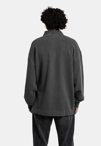 Overdimensioneret mørkegrå sweatshirt med krave, struktureret stof, sænkede skuldre og en lige kant. Bagfra vises der minimale syninger.
