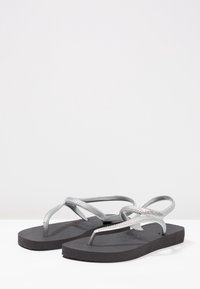 Harmaat flip flop -sandaalit, joissa on teksturoidut remmit ja musta kumipohja. Remmeissä on kudottu kuvio lisäyksinä.