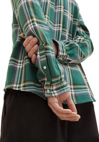 Grünes karriertes Button-Up-Hemd mit weißen, lila und orangefarbenen Akzenten. Lange Ärmel mit Knopfärmeln und einer lockeren Passform, gefertigt aus weichem Stoff.