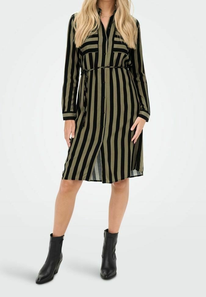 Femme portant une robe boutonnée à rayures verticales noires et vert olive avec une ceinture à la taille et des bottines noires.