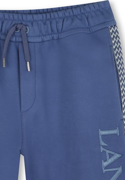 Blauwe joggingbroek van zacht materiaal met een elastische tailleband, trekkoord en zigzagpatroon aan de zijkanten. Voorzien van geborduurde letters.