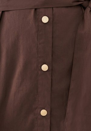 Robe en tissu marron avec une rangée de boutons dorés et une taille nouée, offrant une texture lisse et des lignes épurées.