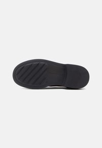 Black rubber shoe sole with a textured tread pattern, featuring horizontal grooves and a rounded heel design. Simple, functional style.