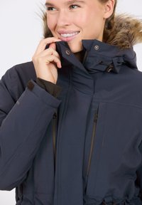 Dunkelblaue isolierte Jacke mit einer kapuze aus Kunstfell, ausgestattet mit zwei Reißverschlusstaschen, verstellbarem Kordelzugbund und hohem Kragen.
