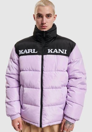Puffjakke med sort overdel og lavendel underdel. Den har høj krave, lynlås og store broderede logoer på forsiden.