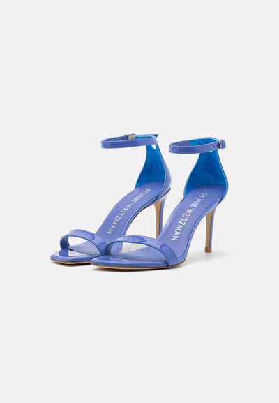 Sandales en cuir verni bleu avec une bride au niveau de la cheville, bout ouvert et un talon aiguille fin. La semelle est beige, avec une texture lisse.