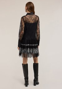 Spitzenkleid mit einem schwarzen durchsichtigen Oberteil, plissiertem Rock und silbernen Akzenten. Kombiniert mit knielangen schwarzen Boots im Krokodil-Prägung.