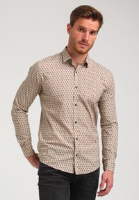 Camisa de manga larga con botones que presenta un patrón geométrico en beige y marrón, cuello clásico y botones negros. Fabricada en tela suave.