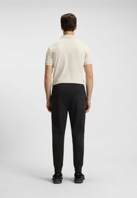 Miesten asu, jossa on vaalean kermavärinen polo-paita ja mustat suppilat housut nilkkaripsillä. Materiaali näyttää sileältä; vähäinen yksityiskohtaisuus näkyy.