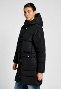 Sort oppustelig jakke med hætte, der har et quiltet design, frontknapper og to forlommer. Fremstillet af glat, vandtæt materiale.