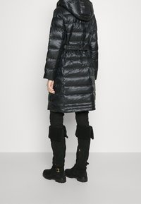 Svart vadderad kappa med huva, åtsittande midja och långa ärmar. Matchad med svarta strukturerade byxor och knähöga svarta stövlar med detaljer.