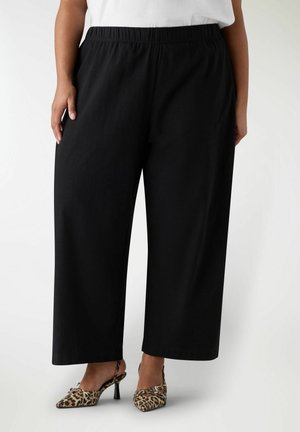 Una persona indossa pantaloni neri larghi e ampi con vita elasticizzata e scarpe slingback con tacco alto a stampa leopardata.