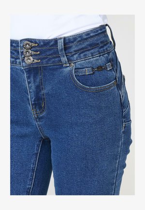 Jeansy dżinsowe z wysokim stanem w ciemnoniebieskim kolorze, z trzema guzikami na górze, kontrastowym przeszyciem oraz przednimi kieszeniami z ozdobnym okuciem.