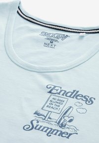 Ljusblå bomull t-shirt med rund halsringning, svart och vit randig detalj, samt ett grafiskt tryck av Snoopy med text.