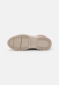 Semelle de chaussure beige clair avec un motif de traction en caoutchouc texturé. Présente une forme arrondie et des bords renforcés. Comprend le logo de la marque.