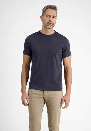 Dunkelblaues T-Shirt mit kurzen Ärmeln aus weichem Stoff, mit rundem Ausschnitt und kleinem Logo auf der Brust, kombiniert mit beigen Hosen.