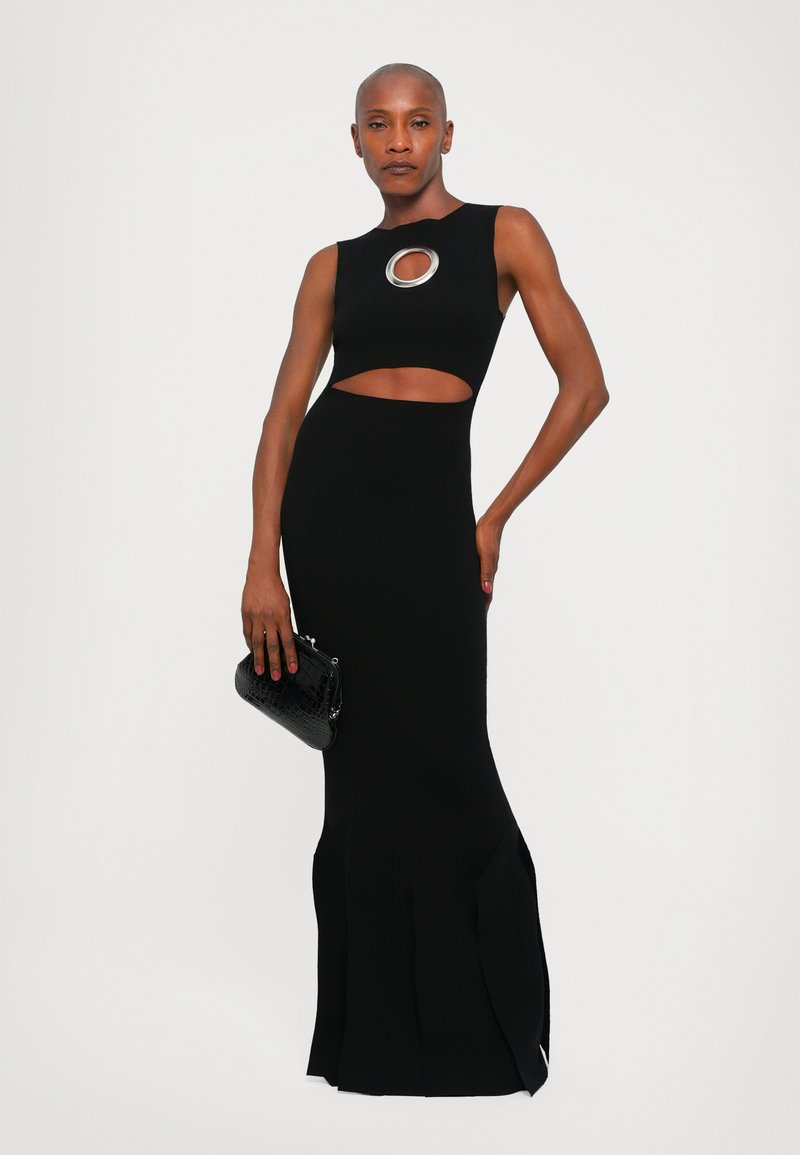 Black knit dress with a cutout under the bust, featuring a circular silver accent. Fitted silhouette with a flared hem and side slits.