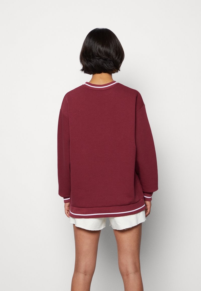 Sudadera burdeos con mangas largas, cuello y puños acanalados, franjas blancas decorativas en el cuello y el bajo, ajuste holgado, textura suave.