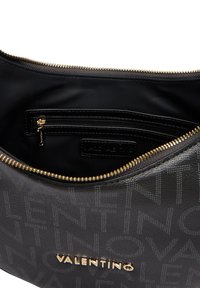 Borsa a mano in pelle nera con motivo logo in rilievo, hardware dorato e una tasca con zip all'interno. Texture liscia e forma arrotondata.