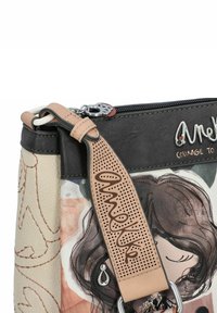 Borsa a spalla in pelle con parte superiore nera, corpo crema, illustrazione stampata e tracolla perforata beige. Gli accessori in argento aggiungono dettagli.
